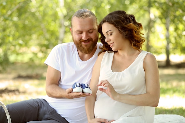 Handsome man and his lovely pregnant wife with blue baby booties  in the park