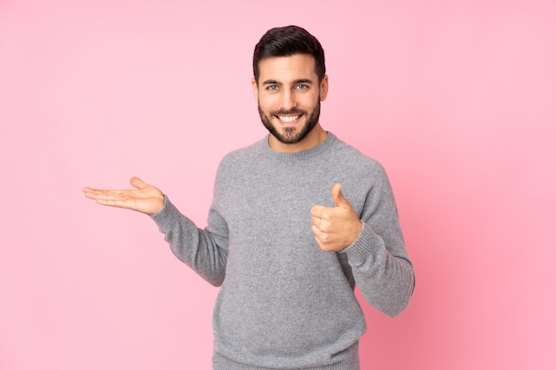 handsome man over holding copyspace imaginary on the palm to insert an ad and with thumbs up