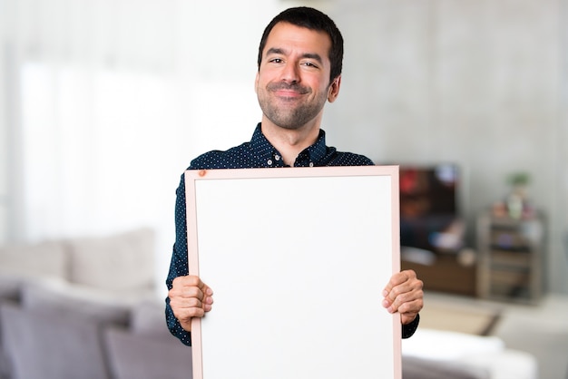 Handsome man holding an empty placard inside house