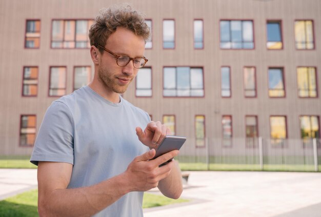 Handsome man holding mobile phone shopping online ordering something standing on the street