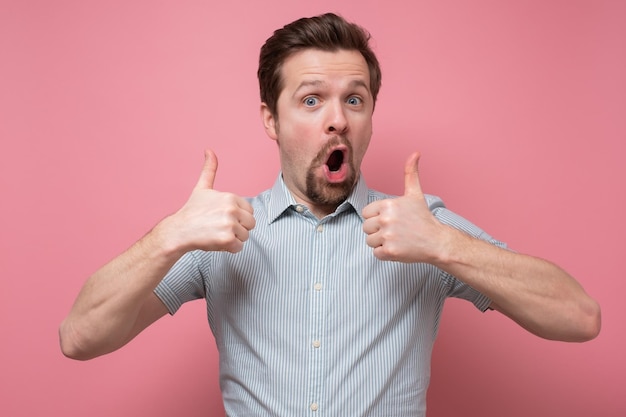 Handsome man holds his thumbs up apporivng his choice Studio shot