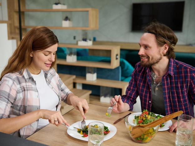 Handsome man husband talks at his beautiful pregnant wife while enjoying delicious healthy lunch together at home