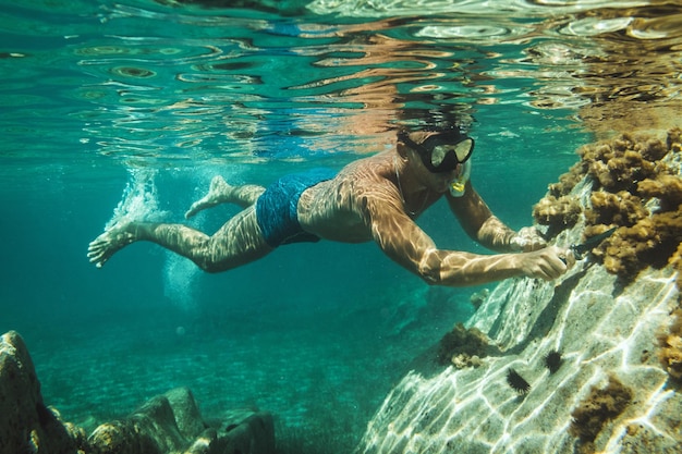 A handsome man is having fun at summer vacation and exploring seafloor during scuba diving in sea.