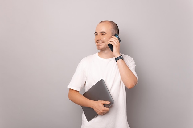 Handsome man is holding closed laptop while smiling and talking on the phone