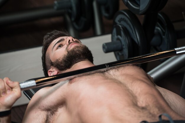 Handsome Man Is Working Out Chest With Barbell In A Modern Gym