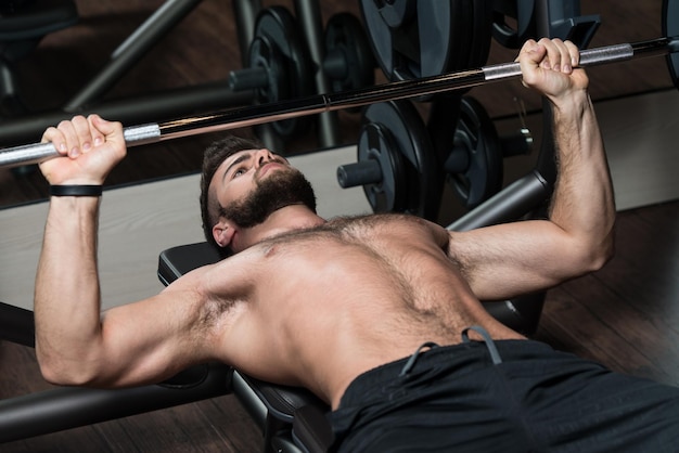 Handsome Man Is Working Out Chest With Barbell In A Modern Gym