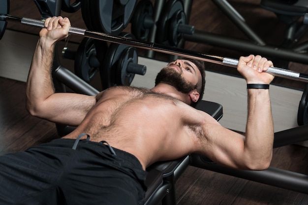 Handsome Man Is Working Out Chest With Barbell In A Modern Gym