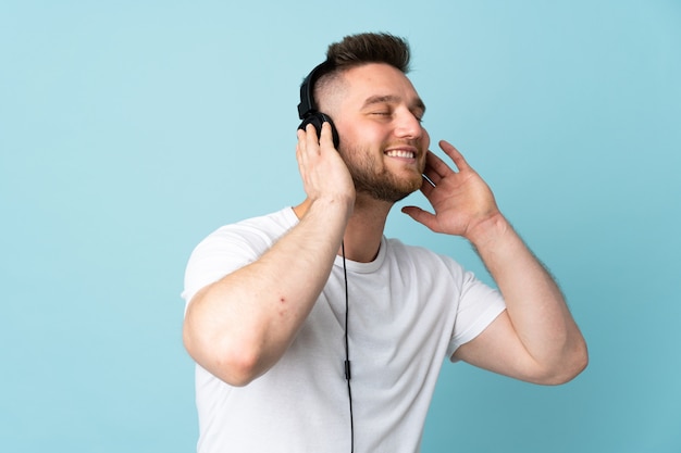 Handsome man isolated on blue wall listening music and singing