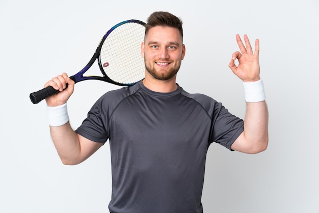 Handsome man isolated on white wall playing tennis and making OK sign