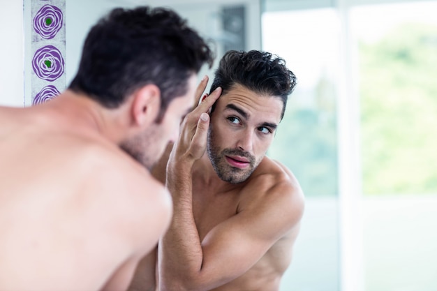 Handsome man looking at his hair in bathroom