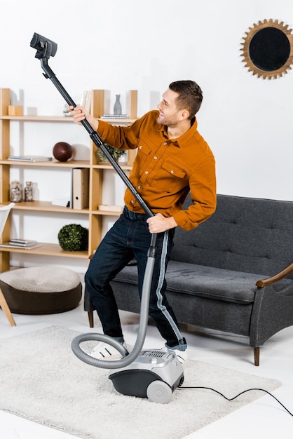 Photo handsome man in modern living room smiling and rising up hoover