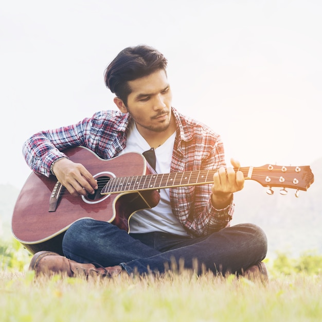 Handsome man playing guitar on green grass