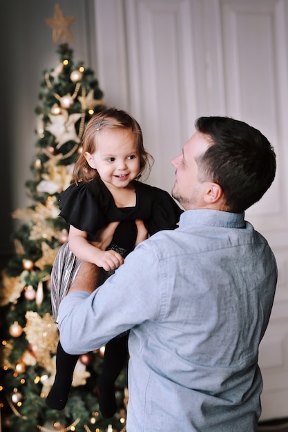 Handsome man plays with his funny daughter near the Christmas tree at home