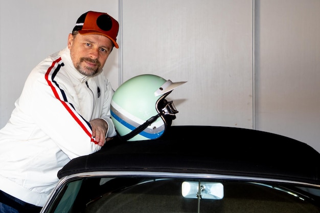 Handsome man portrait of middle aged caucasian guy car race white jacket vintage and retro racing helmet