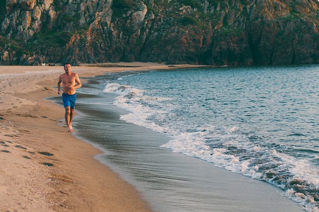 Handsome man running on the sunset beach