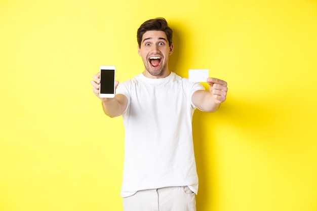 Handsome man showing smartphone screen and credit card