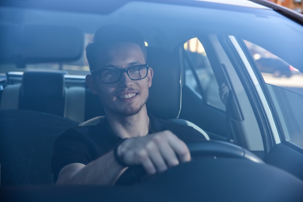 Handsome man sitting in a car and holding steering wheel.