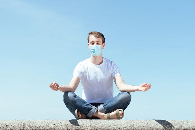 Handsome man sitting in lotus pose outdoors and wearing a protective mask