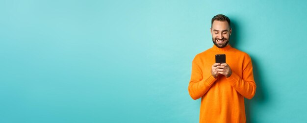 Handsome man smiling and texting message on mobile phone communicating online standing over light bl