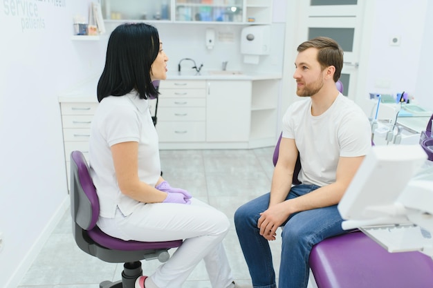 Handsome man smiling while teeth exam Happy male patient sitting in a dentist's chair and having check up teeth