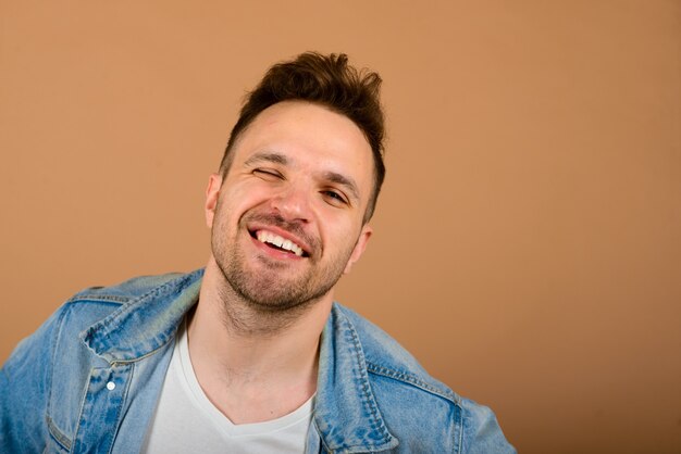 Handsome man standing and smiling isolated on the light brown studio background.