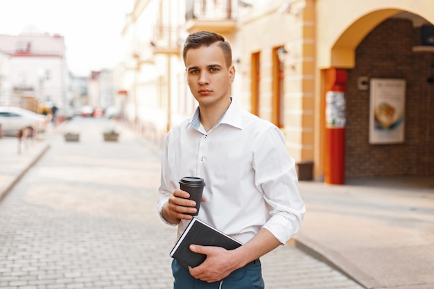 Handsome man in a stylish shirt with coffee and a notebook near the building