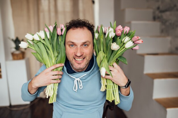 Handsome man in a sweatshirt smiles and holds a bouquet of tulips in his hands