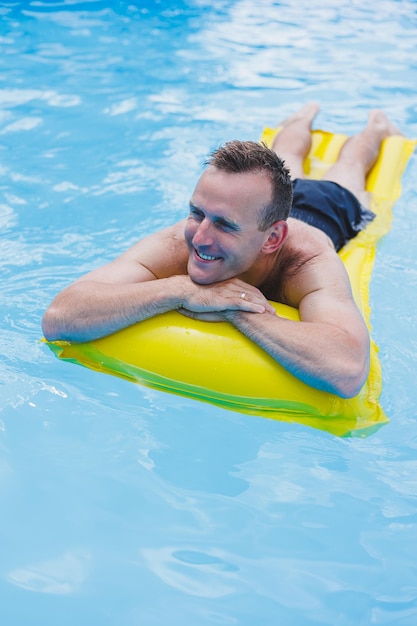 Handsome man in swimming shorts with an inflatable yellow mattress in the pool Summer vacation in the hotel