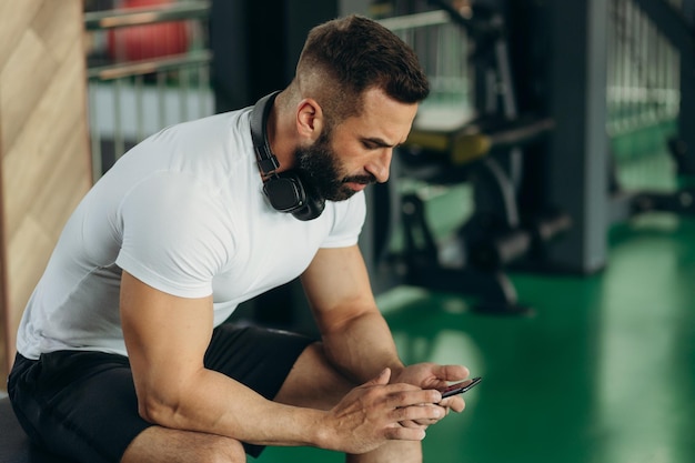 Handsome man using phone while having exercise break in gym