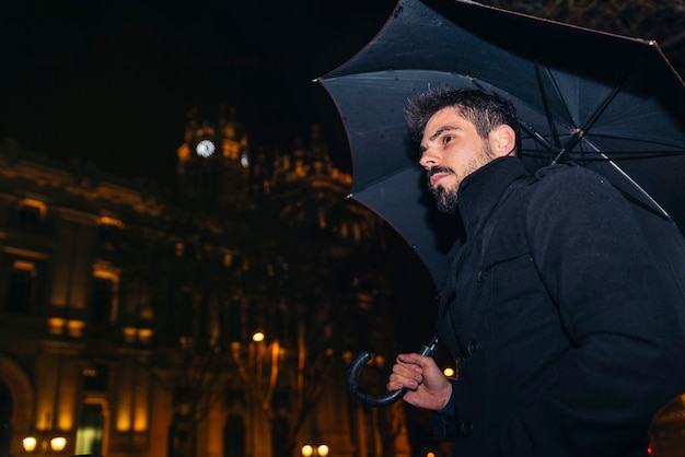 Handsome man walking in Madrid at night in the rain.