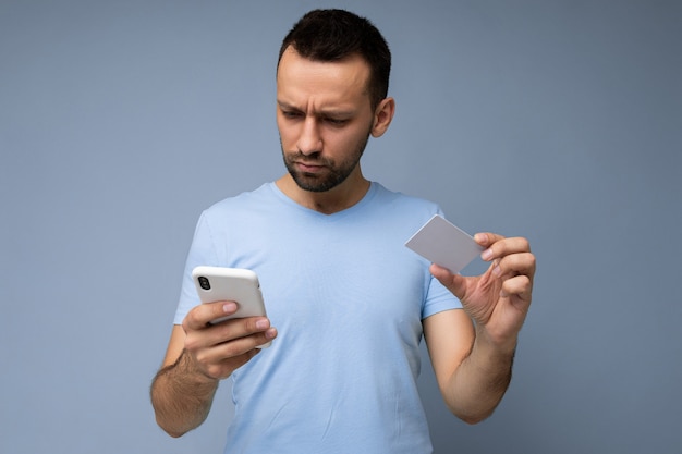 Handsome man wearing everyday clothes isolated on background wall holding and using phone and credit