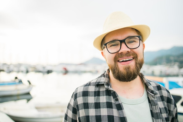 Handsome man wearing hat and glasses near marina with yachts Portrait of laughing man with sea port background with copy space