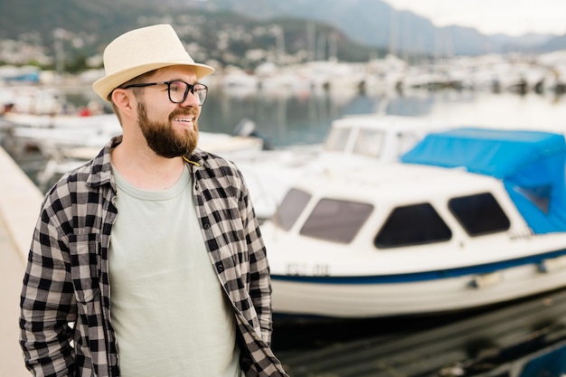 Handsome man wearing hat and glasses near marina with yachts Portrait of laughing man with sea port background with copy space