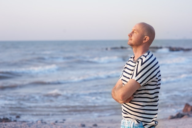 Handsome man wearing a striped t-shirt breathing in front of the ocean on beach.