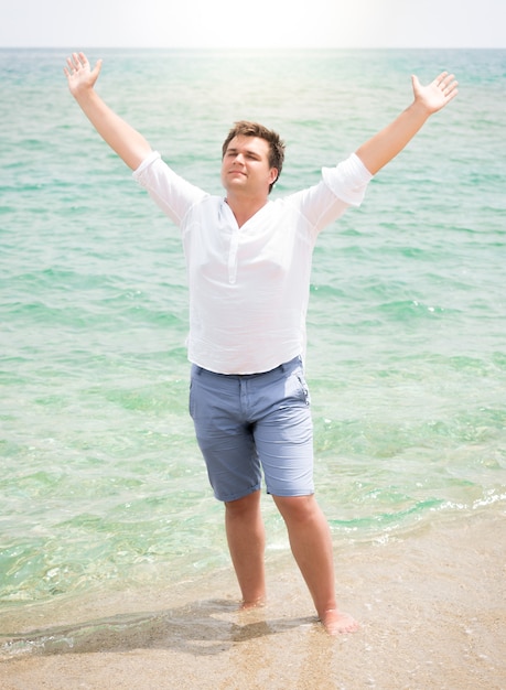 Handsome man in white shirt enjoying sea and raising hands in the sky