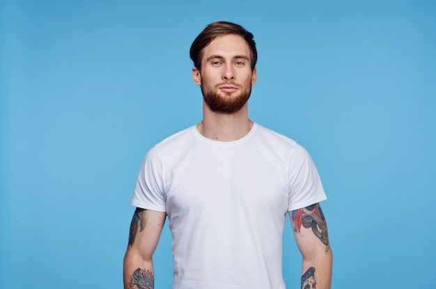 Handsome man in white tshirt tattoos on his arms cropped view blue background