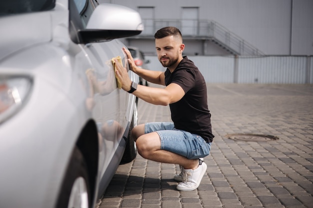 Handsome man wipes a car with a rag in a showroom at a selfservice car wash gray car