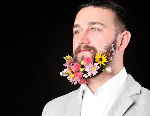 Handsome man with beard of flowers on dark background