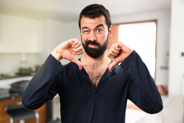 Handsome man with beard making bad signal inside house