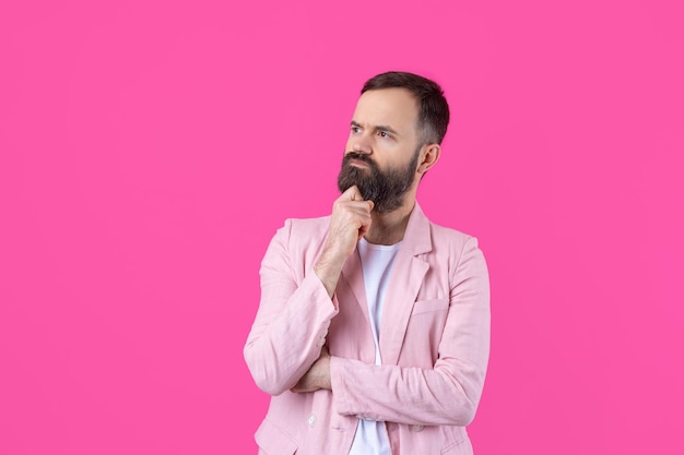 Handsome man with a beard in a pink jacket is thinking over an isolated red background