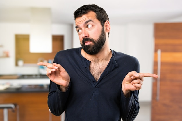 Handsome man with beard pointing to the laterals having doubts inside house