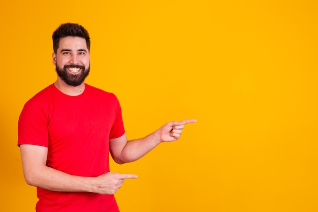 Handsome man with beard pointing to the side smiling looking at the camera.