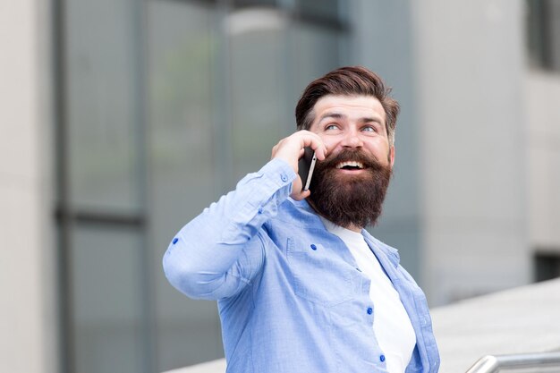 Handsome man with bristle outdoors. Man wearing casual shirt hold smartphone. Modern life. Agile business. Thanks. How are you doing. Mobile communication. Business conversation. Man with smartphone.