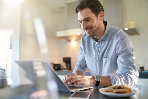 Handsome man with computer in modern kitchen                                                     