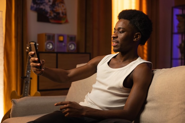 A handsome man with dark skin relaxes on a couch in a sunsetlit living room