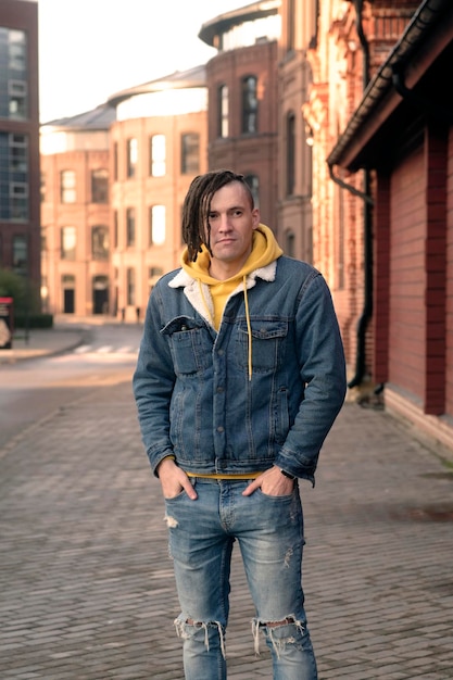 Handsome man with dreadlocks posing on city street Positive male looking away smiling