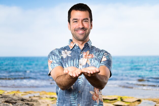 Handsome man with flower shirt holding something at the beach