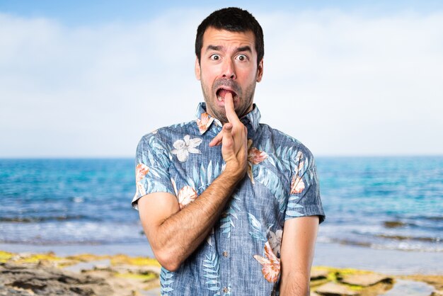 Handsome man with flower shirt making suicide gesture at the beach