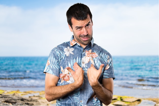 Handsome man with flower shirt making surprise gesture at the beach