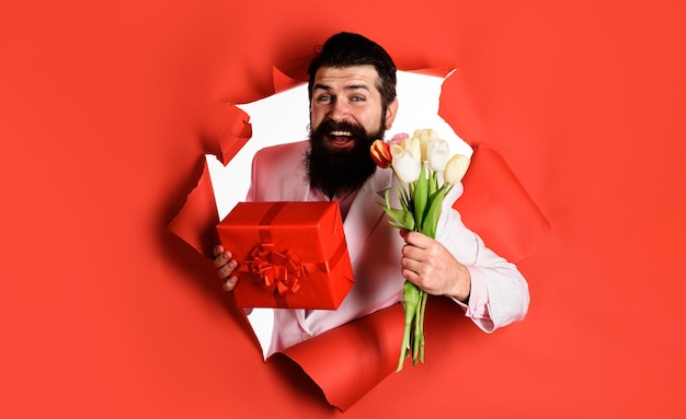 Handsome man with gift box and bouquet of flowers businessman with gift and tulips looking through